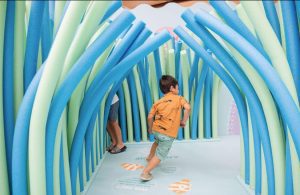 A child running through a maze display full of blue and green pool noodles.