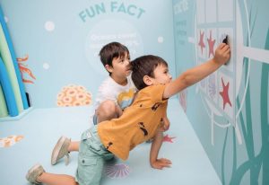 Two children playing naughts and crosses on a Re-Board display with flat magnetic shells and starfish instead.